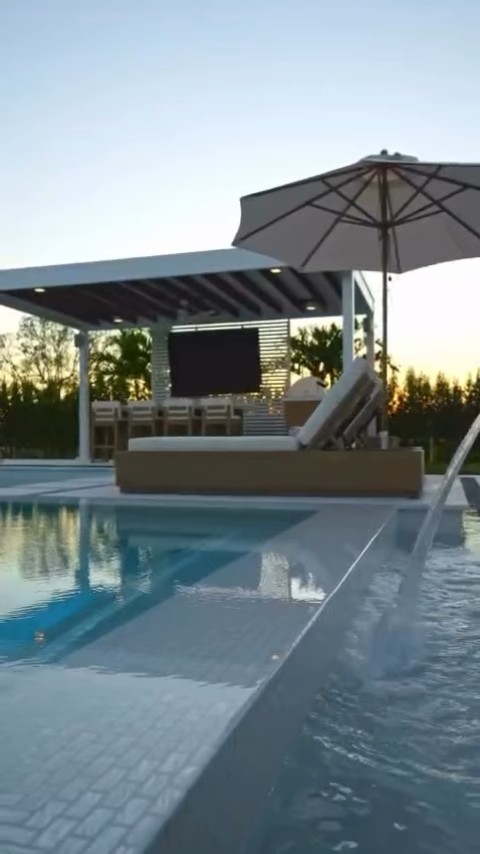 Luxury pool with covered pergola and water feature at sunset in Davie, FL