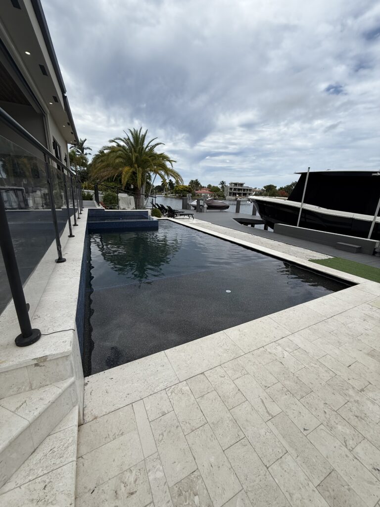 Dark-water canal-front infinity pool with glass railing and yacht dock in Lighthouse Point, FL