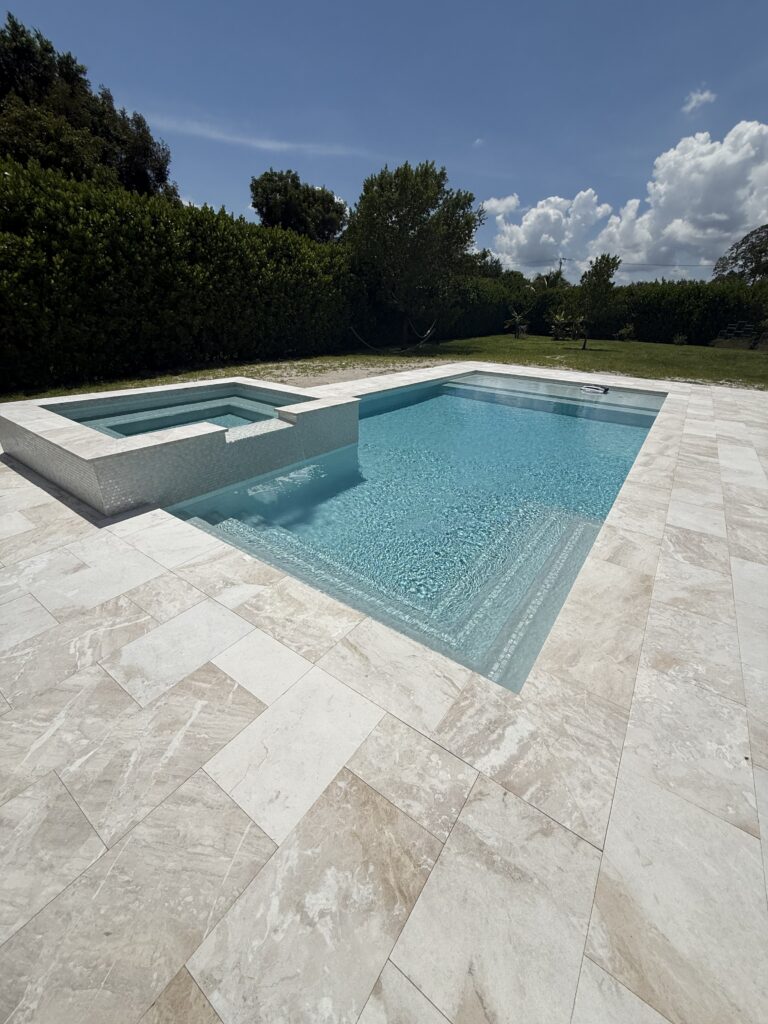 Rectangular pool with raised spa and travertine decking in Plantation, FL