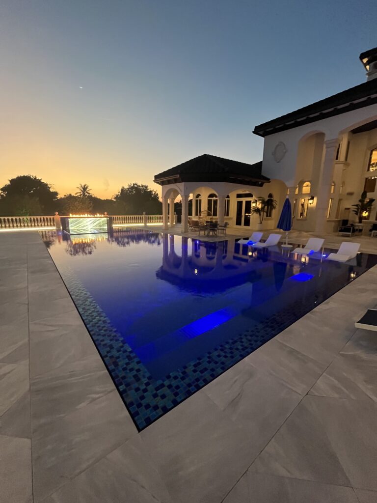 Twilight infinity-edge luxury pool with linear fire feature wall in Southwest Ranches, FL