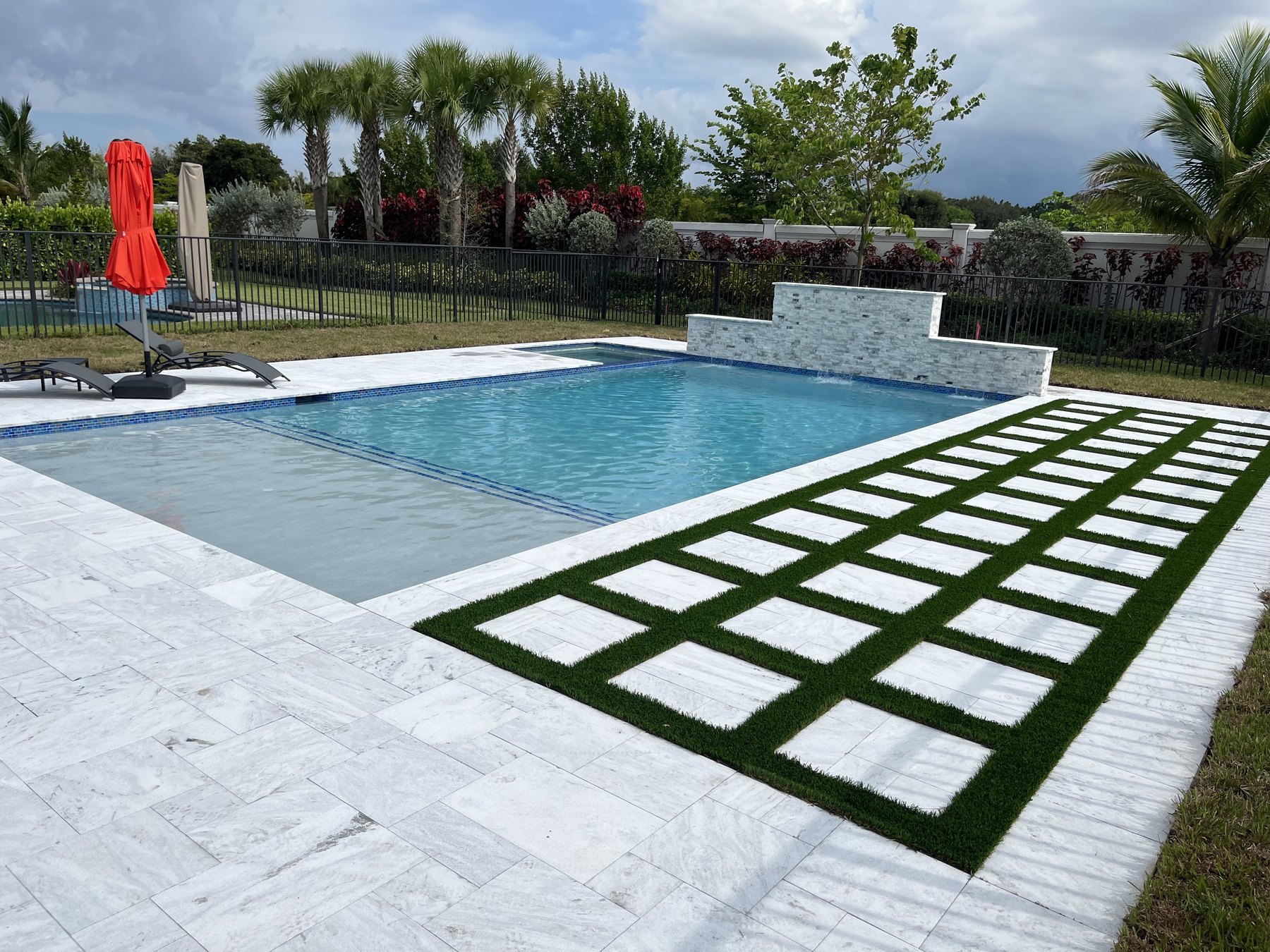 Marble pool deck with synthetic turf inlay, raised stone water feature wall and sun shelf on a Custom Watershapes project in Broward County, Florida