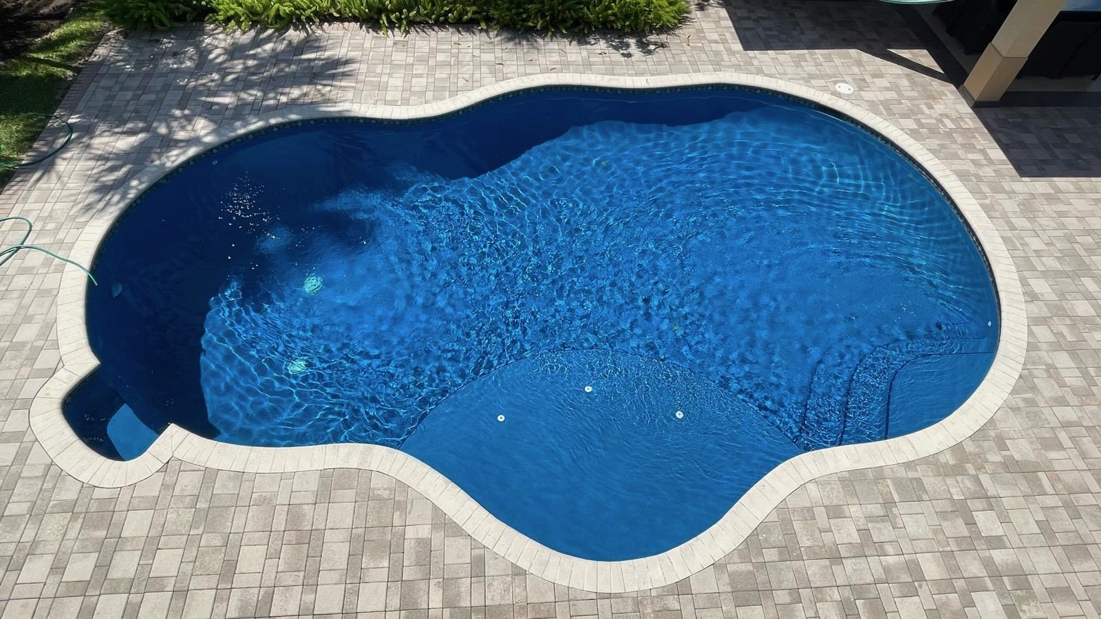 Freeform pool with a deep blue interior finish and paver deck in Weston, Florida